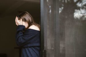 Female suffering Generalised Anxiety Disorder leaning against a door, having her hands over her face.